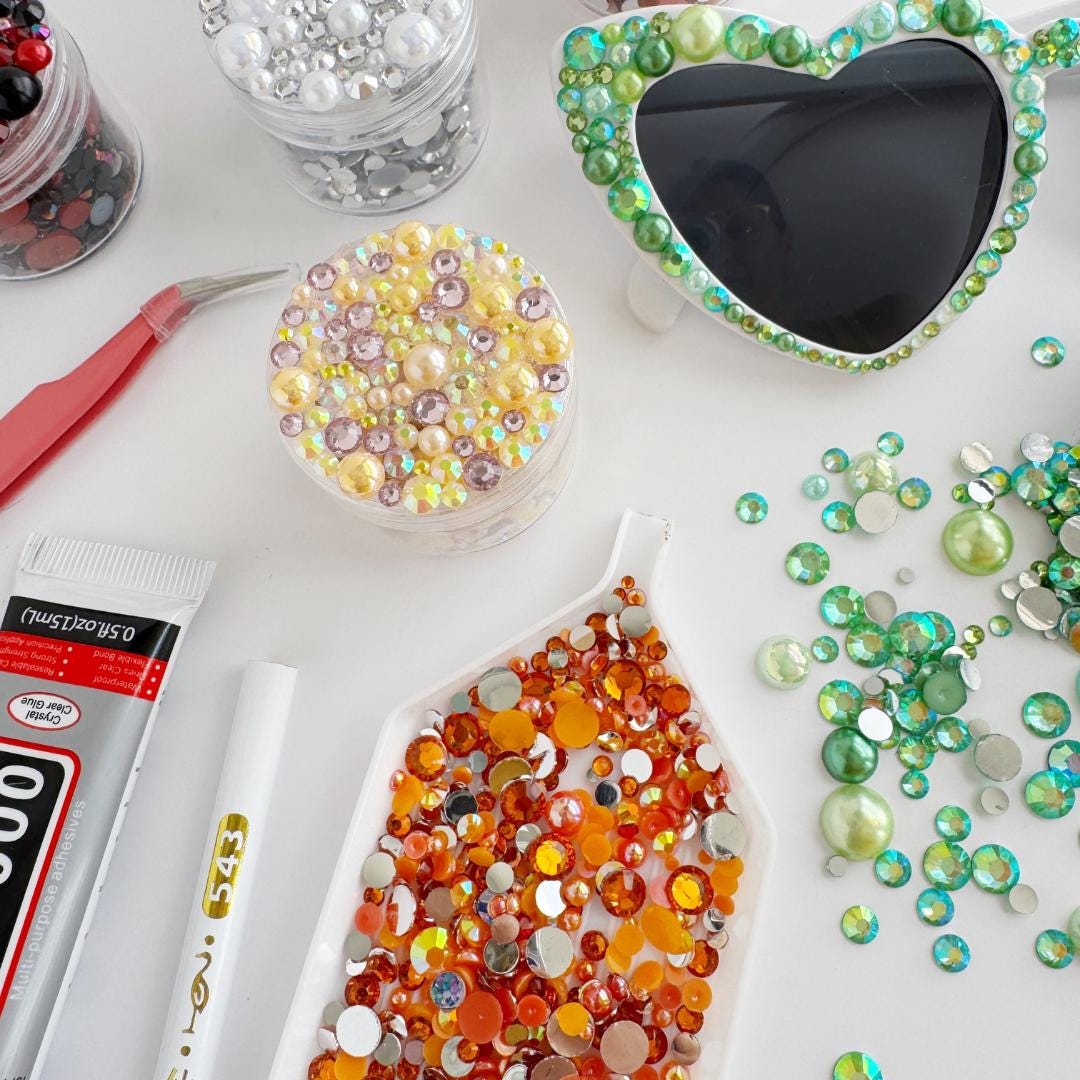 various craft supplies, including a pair of colorful beads, a pair of sunglasses with a heart-shaped frame, and a pair of scissors.
