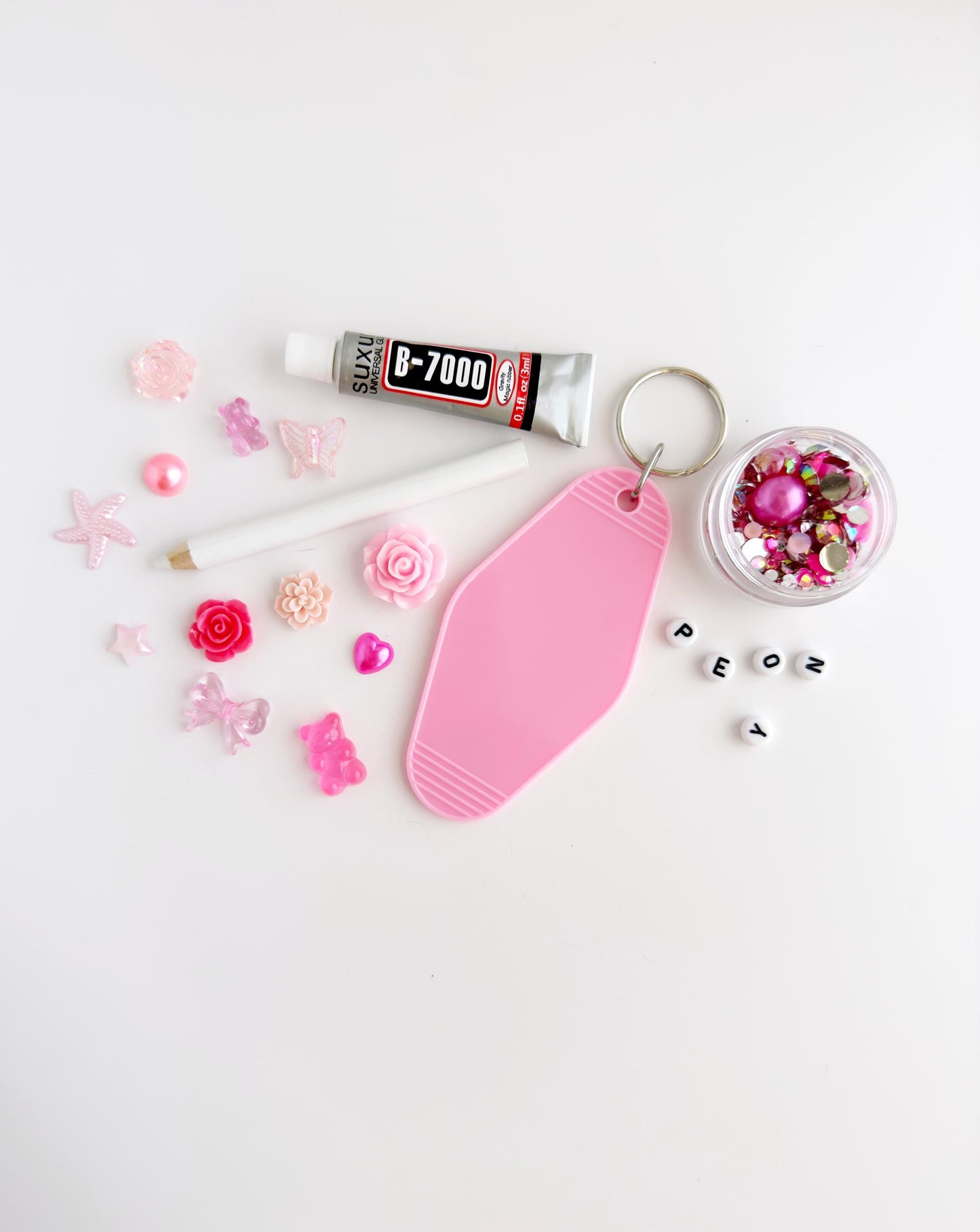 various pink and white items, including a tube of glue, a keychain, a small bowl of glitter, and a collection of small objects such as beads and flowers.