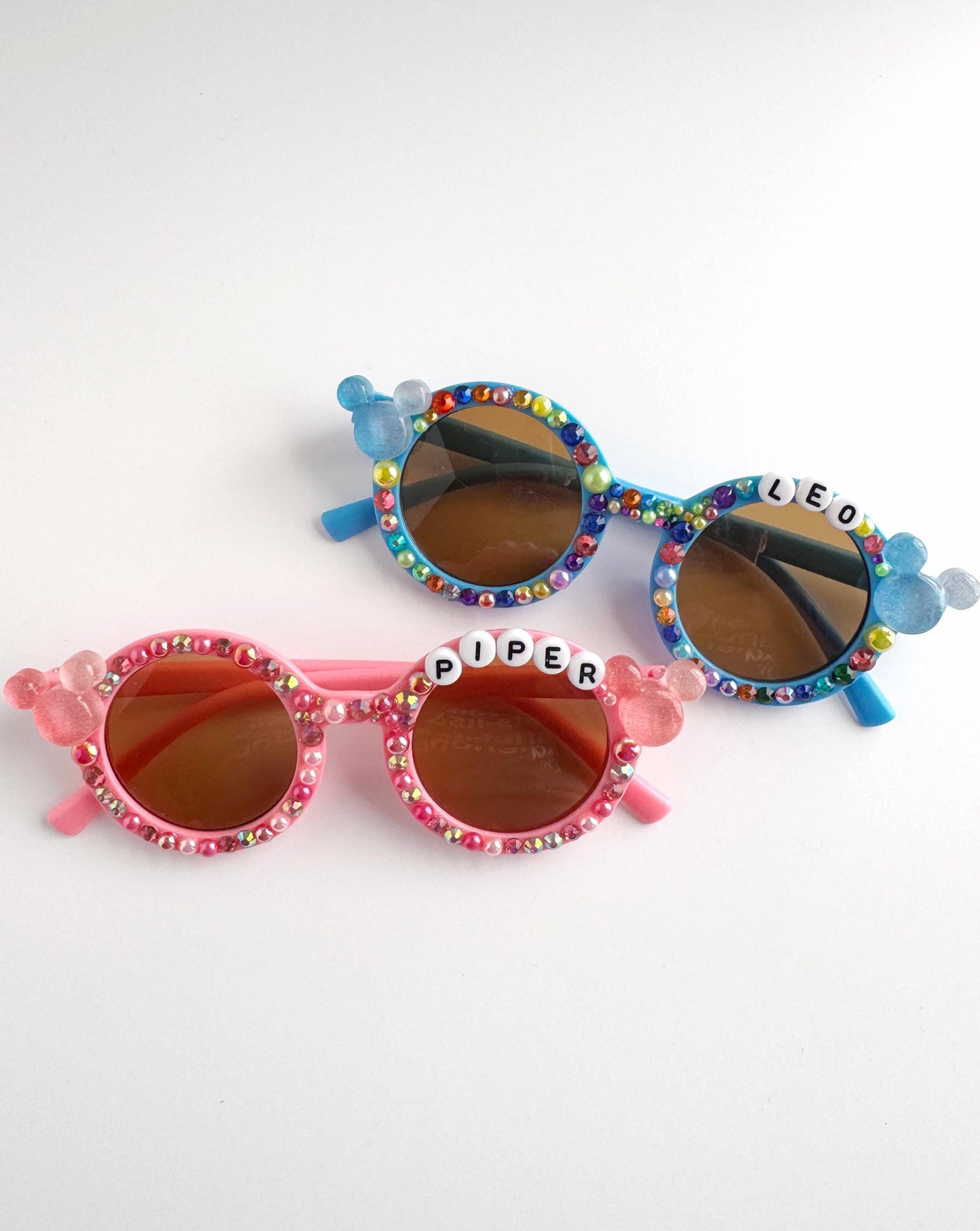 A pair of colorful, personalized sunglasses with the names "LEO" and "PIPER" engraved on them.