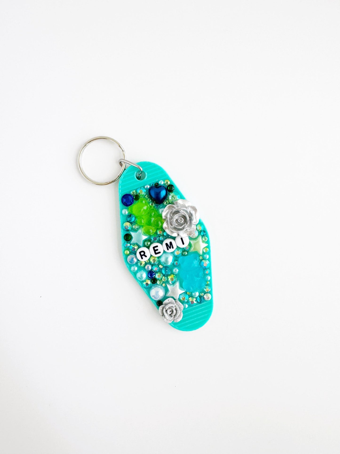 A turquoise keychain with various colorful beads, flowers, and the word "REM" written on it.