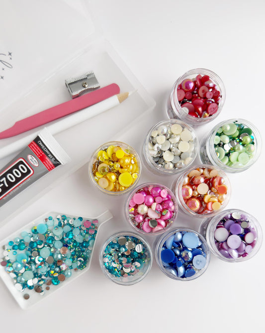 A collection of colorful beads, a pink tool, and a clear container filled with beads are arranged on a white surface.