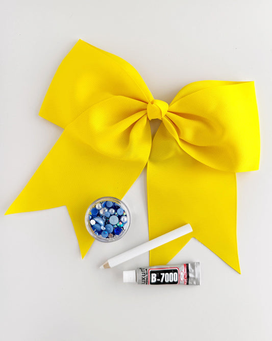 a yellow ribbon, a small bowl of blue beads, a white pencil, and a tube of glue, all arranged on a white background.
