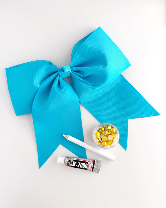 a large blue ribbon, a tube of glue, and a small bowl of colorful beads, all arranged on a white surface.