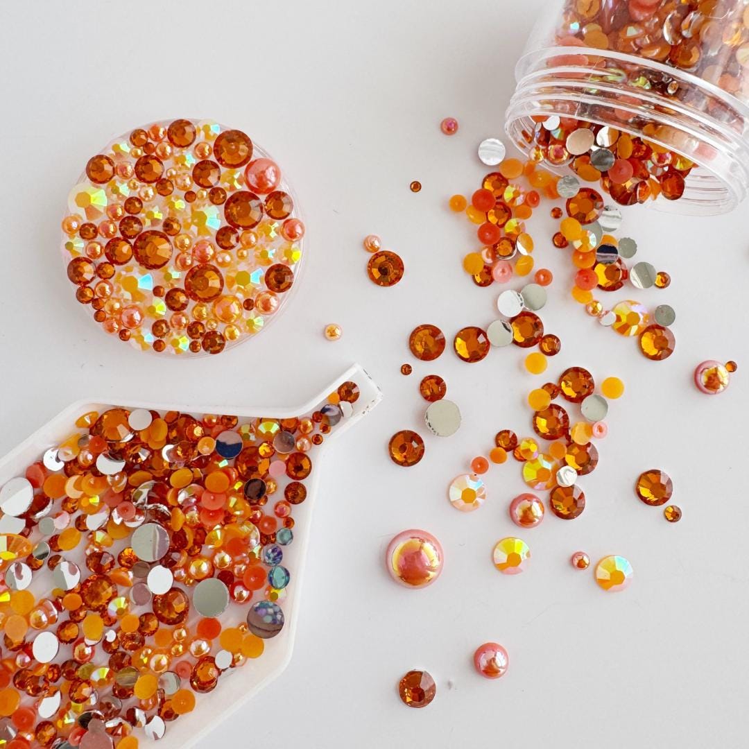 a variety of colorful beads and stones, including orange, yellow, and pink, scattered across a white background.