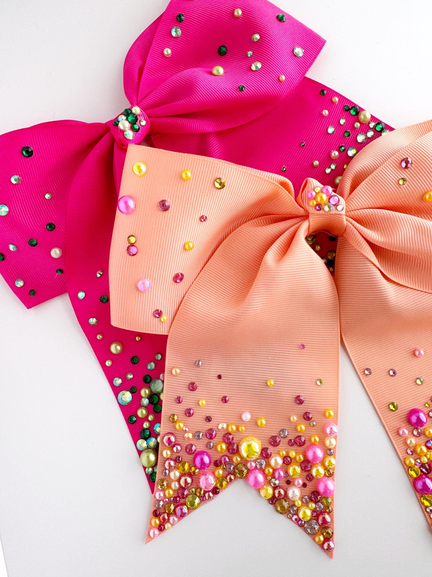 three decorative bows with colorful beads and sequins, including pink, peach, and orange bows, as well as a pink bow with a gold and pink sequin design.