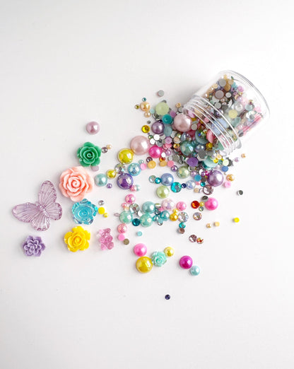 A collection of colorful beads, gemstones, and decorative elements, including flowers and butterflies, scattered on a white background.