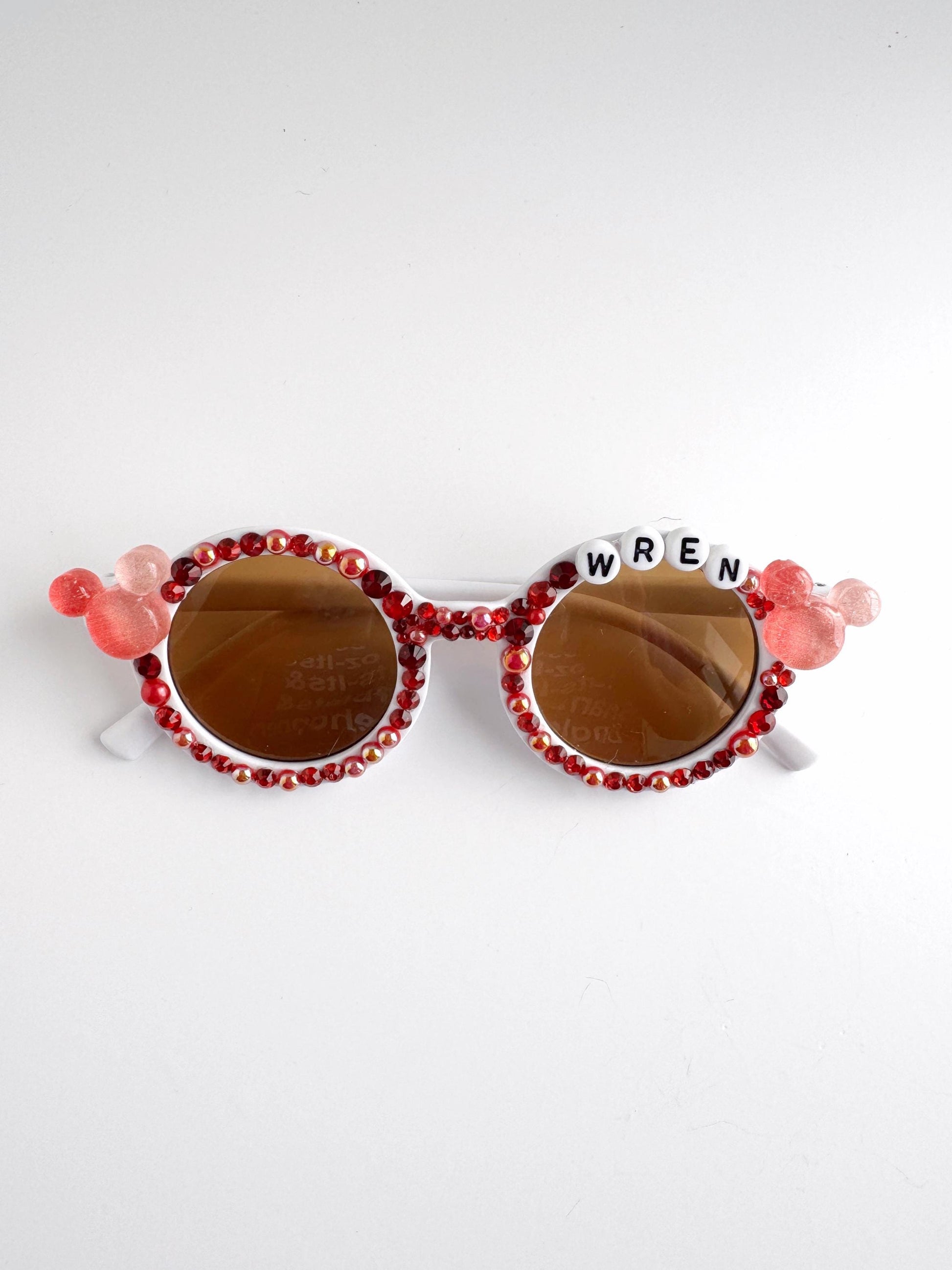 A pair of red and gold sunglasses with the word "WREN" spelled out in white letters on the frame.