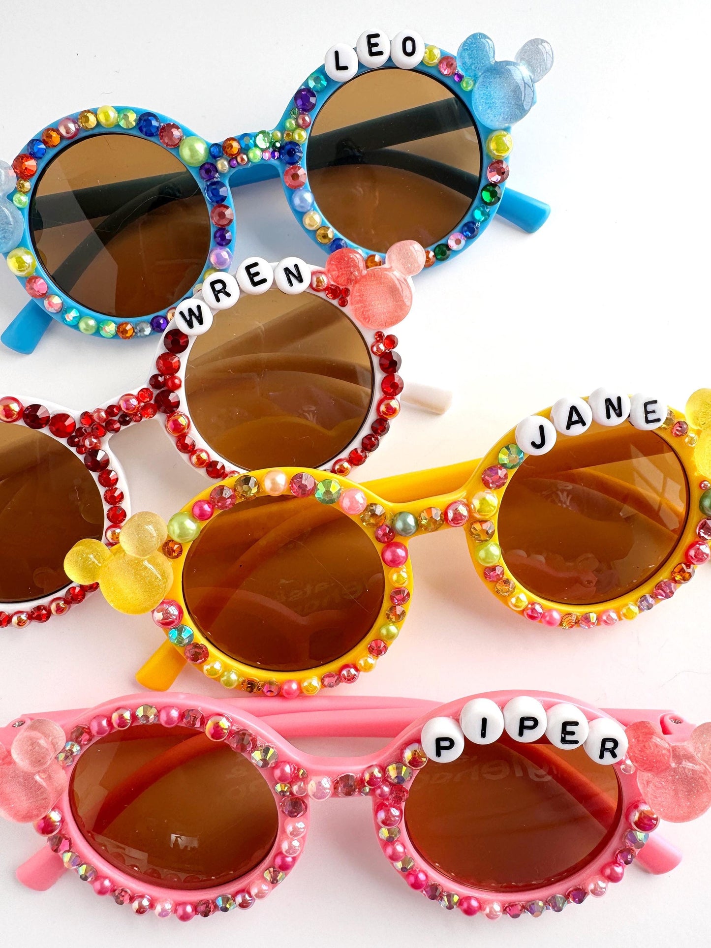 A collection of colorful, personalized sunglasses with rhinestones and name charms.