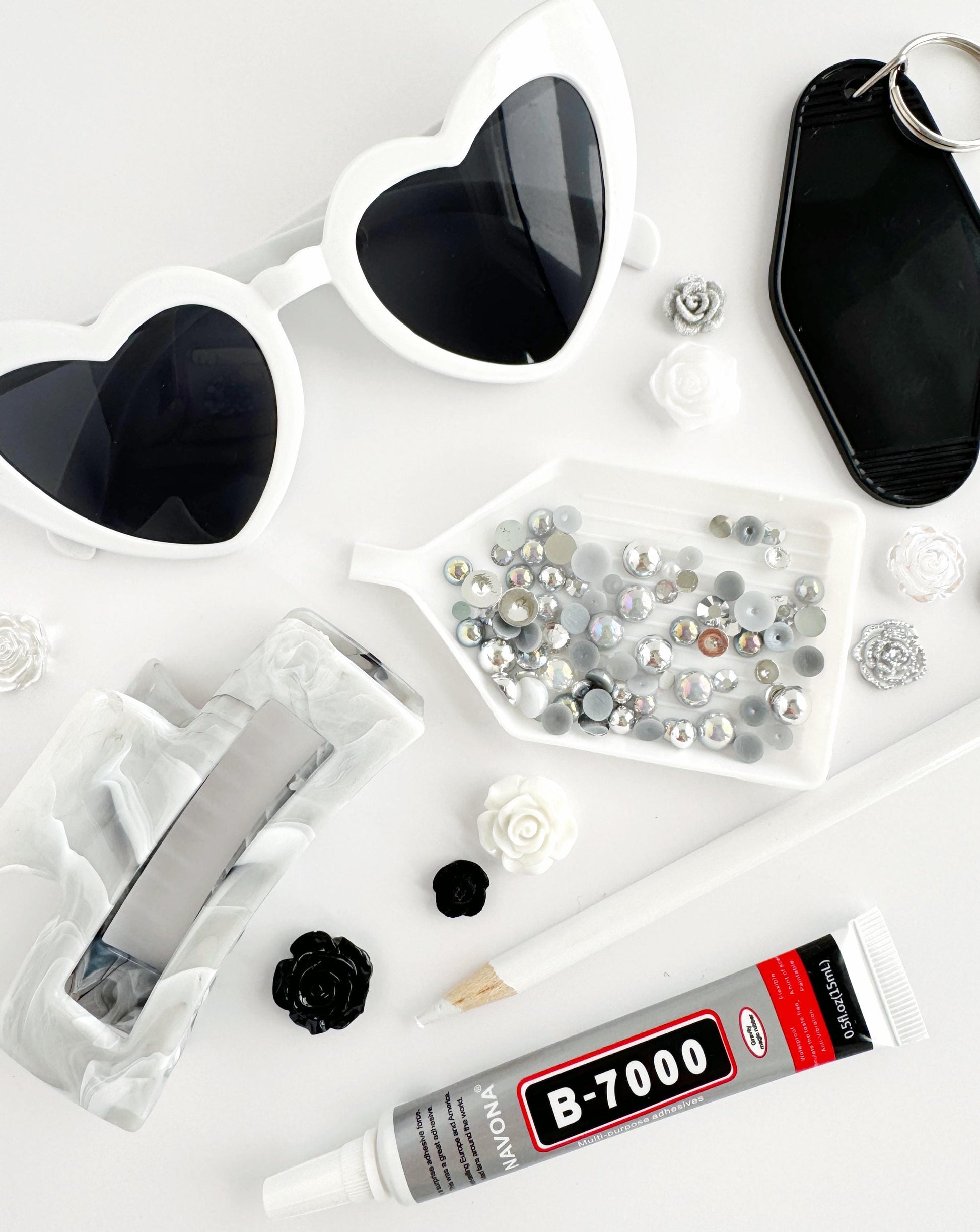 various items, including heart-shaped sunglasses, a keychain, a magnifying glass, a magnifying glass case filled with small silver and white objects, a tube of glue, and some small black and white objects.