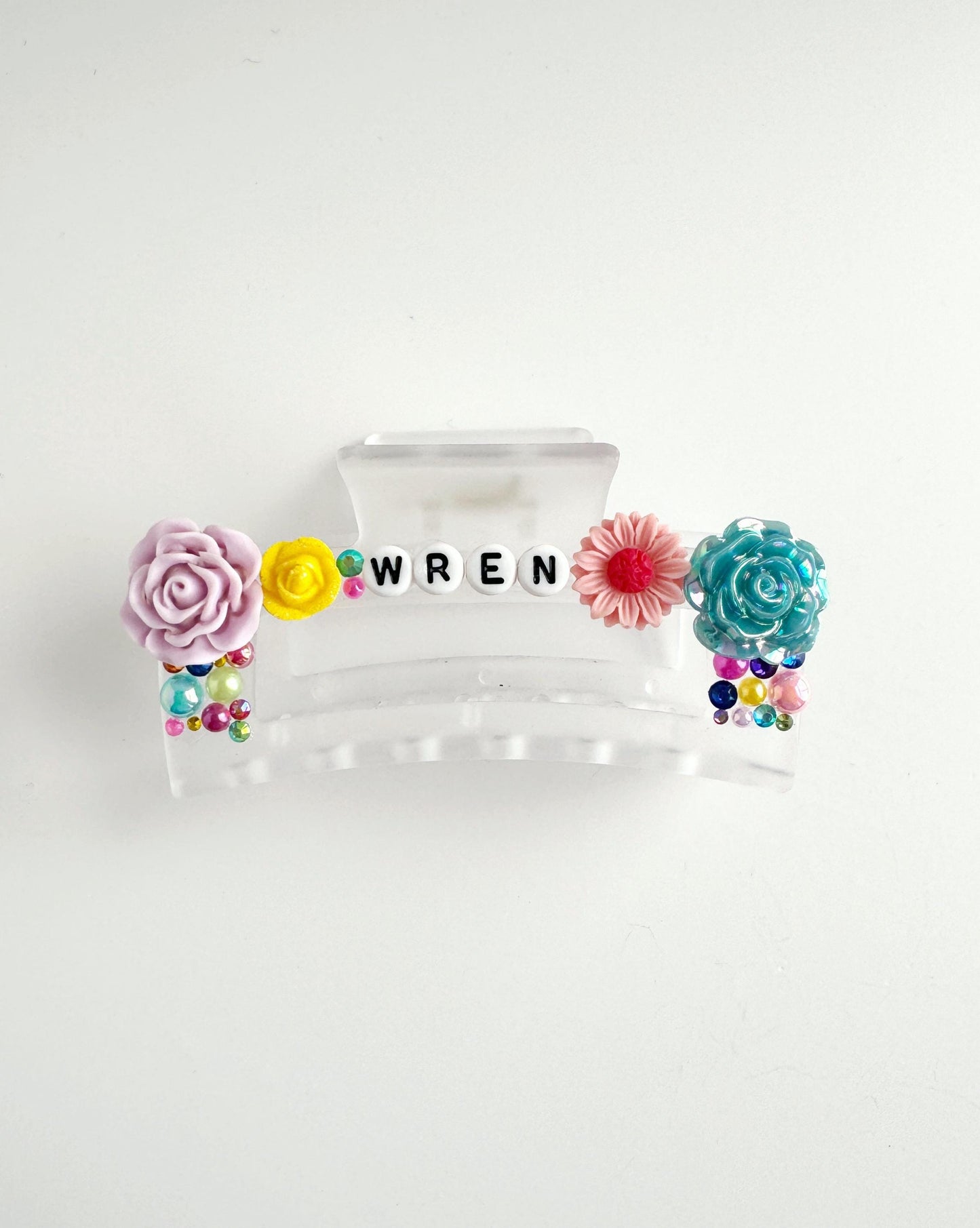 A clear plastic hair clip with colorful flowers and the word "WREN" spelled out in letters.