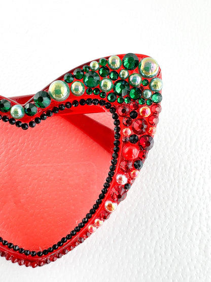 a red and green heart shaped brooch sitting on a white surface